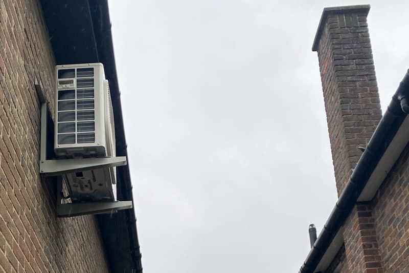External air conditioning uni high up on a wall of a home.