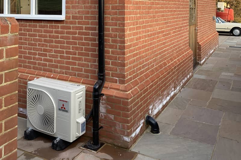 External Mitsubishi air conditioner inverter mounted on a red brick wall.